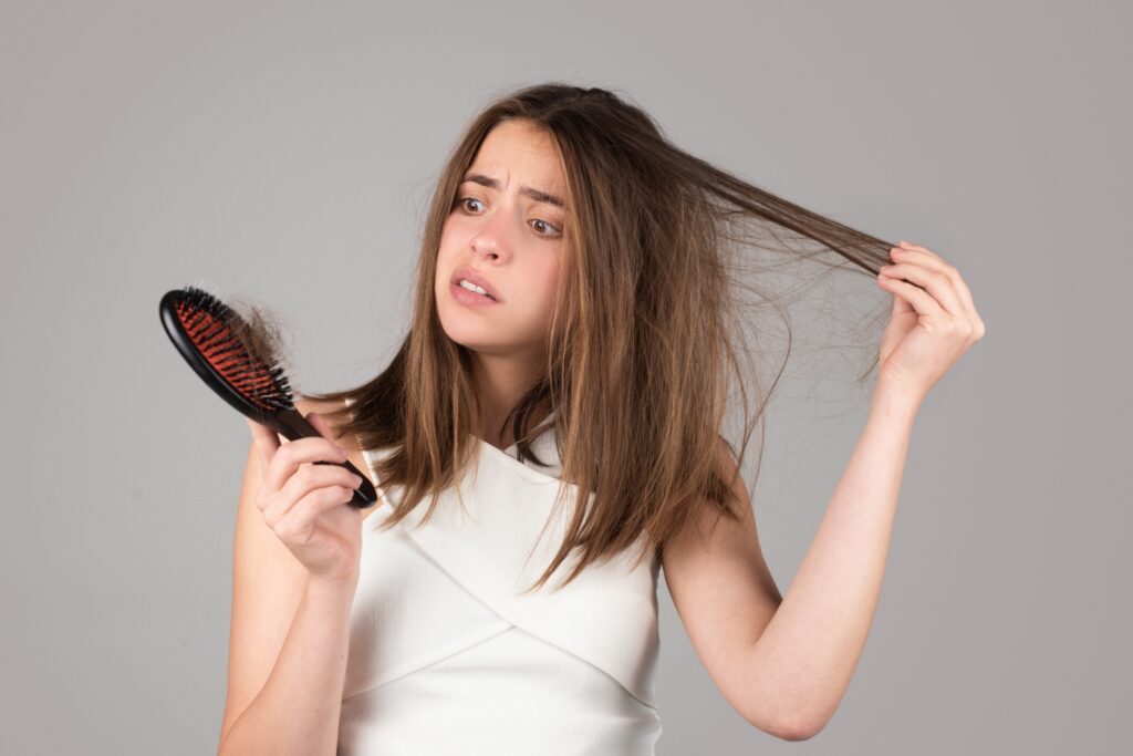 woman looking at her hair brush having loose strands of hair from her head stuck in it